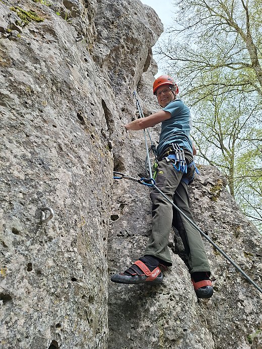 Ein Kletterer mit Helm und Kletterausrüstung steigt eine steile Felswand hinauf und sichert sich mit einem Seil.