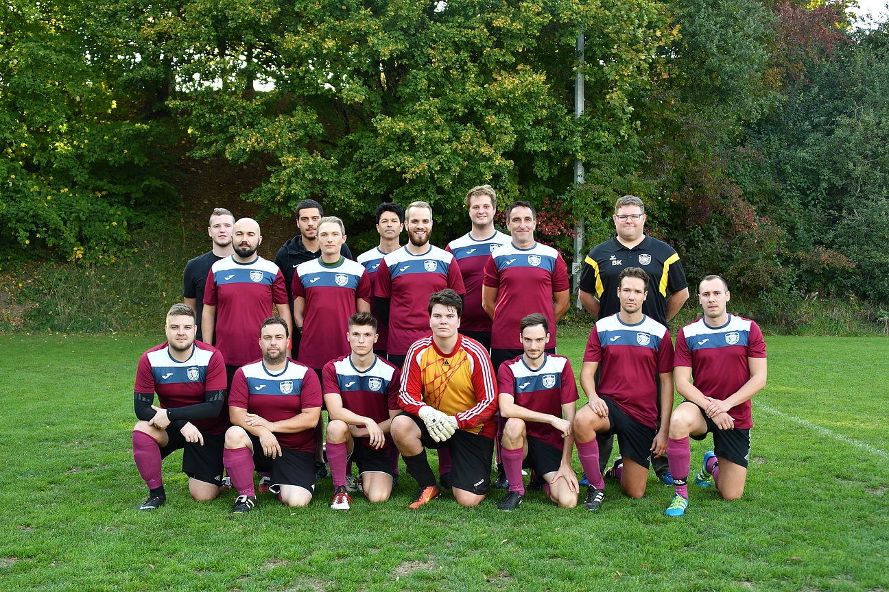 Die 2. Herren Fußballmannschaft des SpVgg Attenkirchen  steht und kniet in zwei Reihen auf einem Rasenplatz für ein Mannschaftsfoto. Die Spieler tragen bordeauxfarbene Trikots mit schwarzen Hosen, ein Spieler trägt ein gelbes Torwarttrikot. Im Hintergrund sind Bäume zu sehen.
